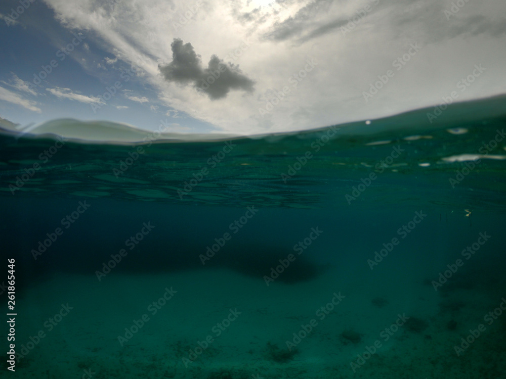 Underwater sea level photo of tropical exotic paradise bay with beautiful blue sky and clouds