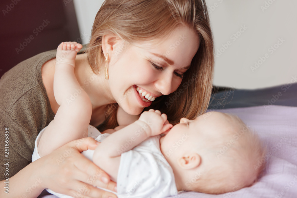 Closeup of young Caucasian woman mother hugging kissing playing with cute newborn baby boy girl child at home. Authentic candid family lifestyle. Happy motherhood and parenting. Closeup of young Caucasian woman mother hugging kissing playing with cute newborn baby boy girl child at home. Authentic candid family lifestyle. Happy motherhood and parenting.