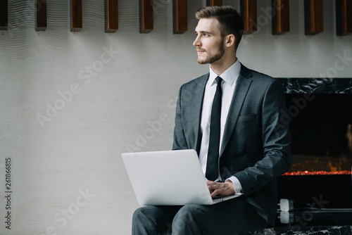Young handsome man sitting in office with cup of coffee and working on project connected with modern cyber technologies. Businessman with notebook trying to keep deadline in digital marketing sphere.