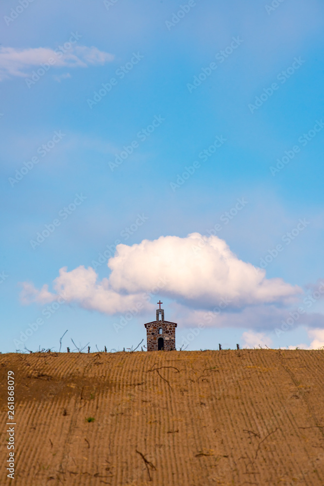 Fototapeta premium A small church sits alone on top of a hill with one puffy cloud above it