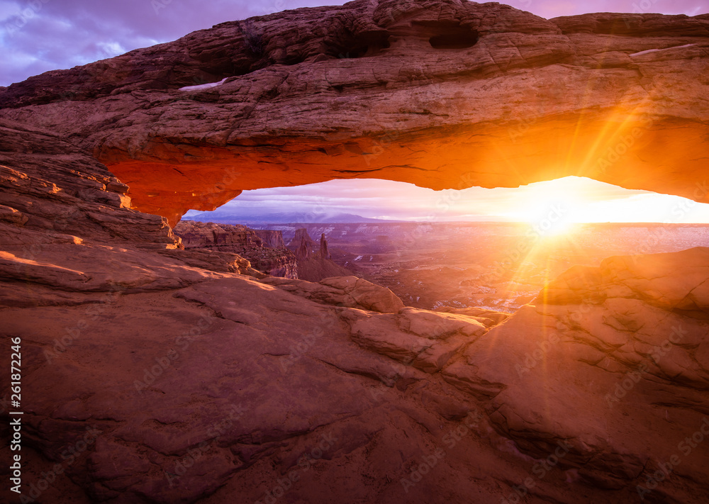 Canyonlands National Park at sunrise as the sun casts an orange glow onto mesa arch.