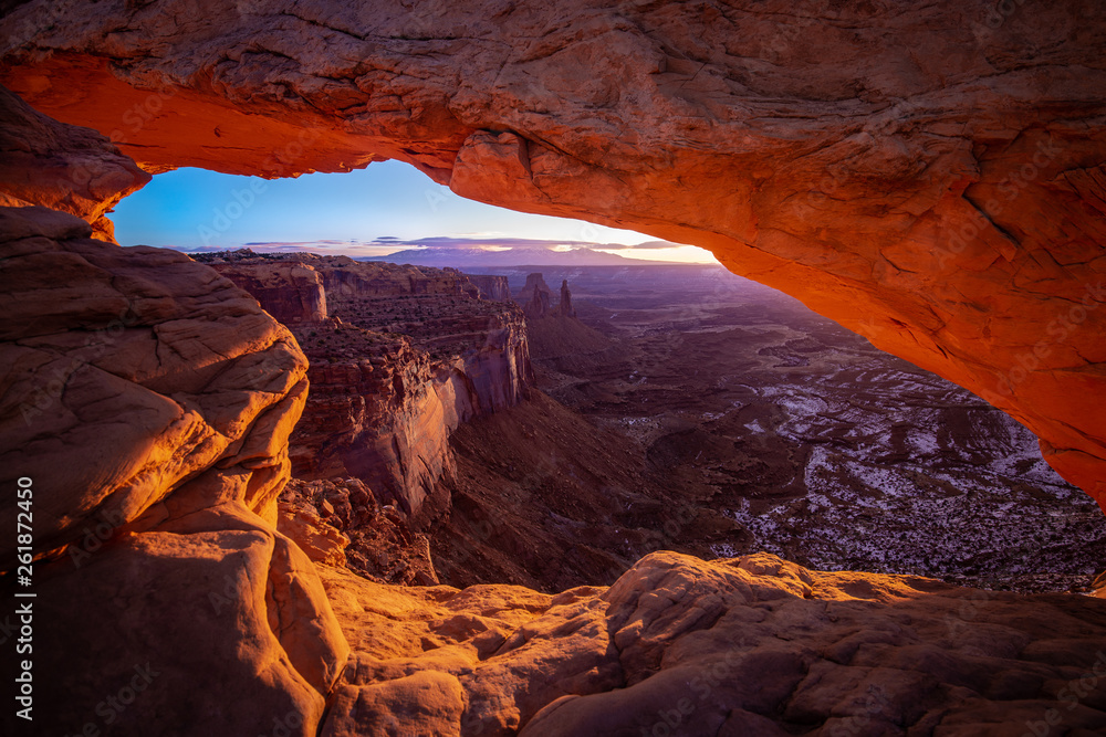 Mesa arch in Canyonlands National Park just outside Moab Utah. The sun creates an orange glow through the window of the desert arch.  The cold snow in the canyon contrasts the orange glow.