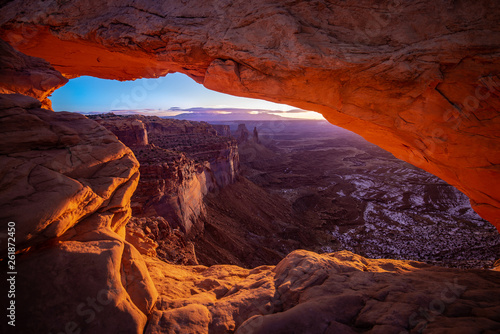 Mesa arch in Canyonlands National Park just outside Moab Utah. The sun creates an orange glow through the window of the desert arch. The cold snow in the canyon contrasts the orange glow.