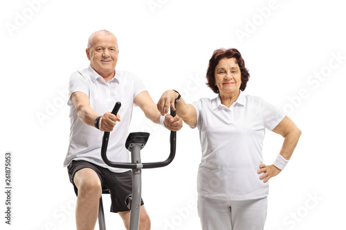 Elderly man exercising on a stationary bike and an elderly woman leaning on it