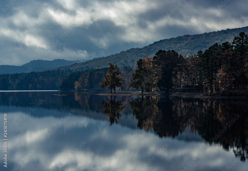 Mirrored reflection on a mountain lake in Northern Arkansas. The adverse weather gives an ominous scene on an early Arkansas Fall morning as the clouds and trees reflect perfectly.