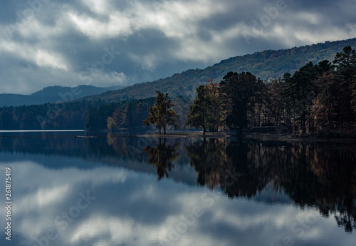 Mirrored reflection on a mountain lake in Northern Arkansas. The adverse weather gives an ominous scene on an early Arkansas Fall morning as the clouds and trees reflect perfectly.