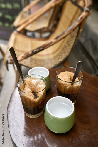Refreshing iced coffee drinks and cups with water on round table outdoors