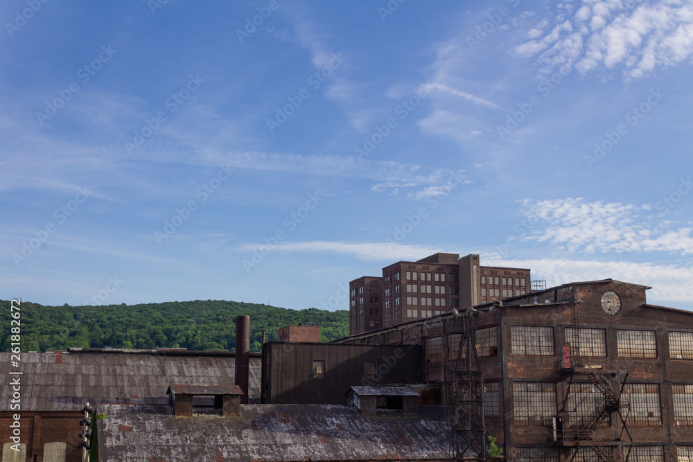 Derelict industrial warehouse with modern commercial building and forested hillside beyond, horizontal aspect