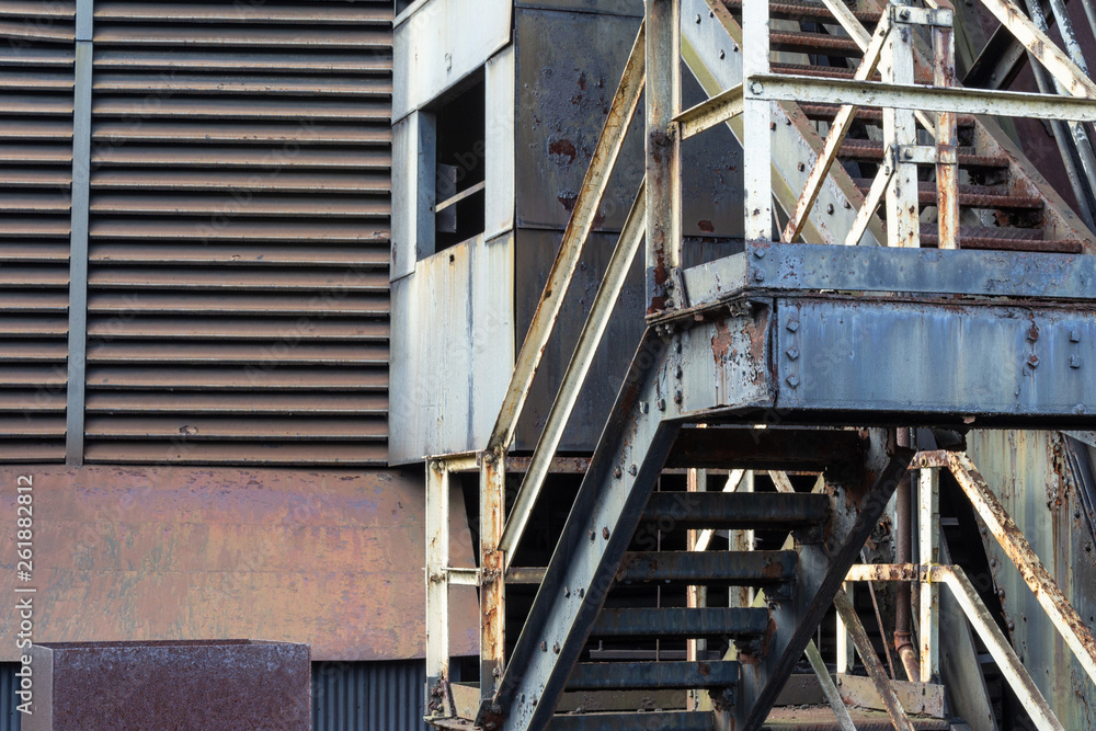 Old industrial stairs, vents, solid and corrugated siding with rust and peeling paint, horizontal aspect