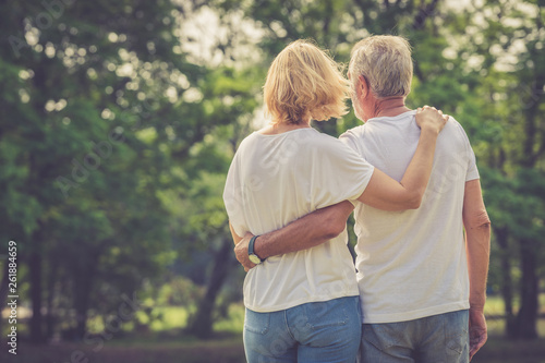 Elder man and woman embrace together looking into the green park