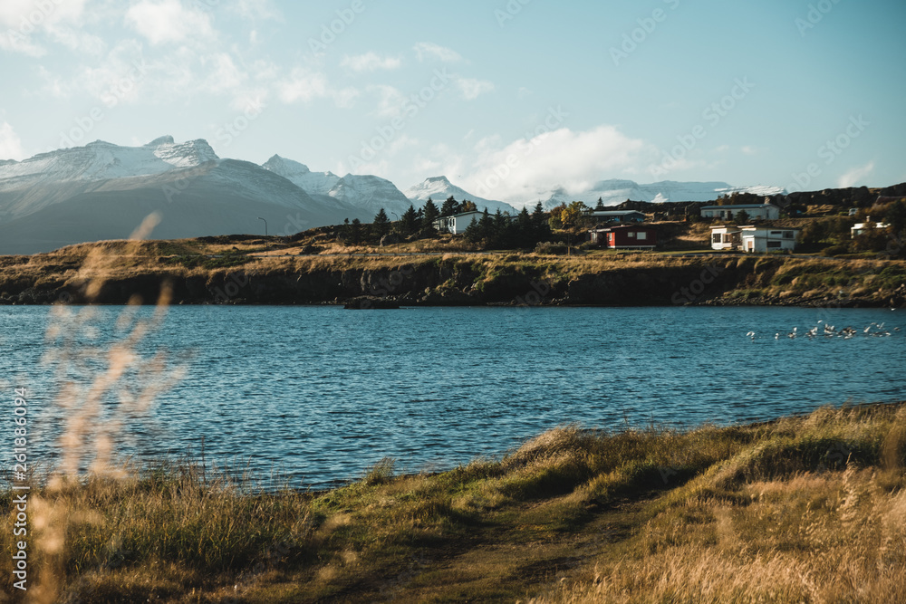 Amazing Iceland landscape with houses and wrack of ship in grass near lake, sunny weather