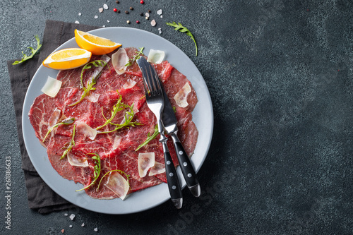 Marbled beef carpaccio with arugula, lemon and parmesan cheese on dark concrete table. Top view, flat lay with copy space