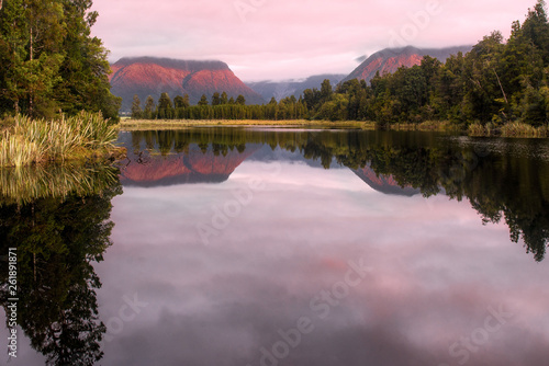 Tree lined lake Matheson reflections at sunset under thick cloud photo