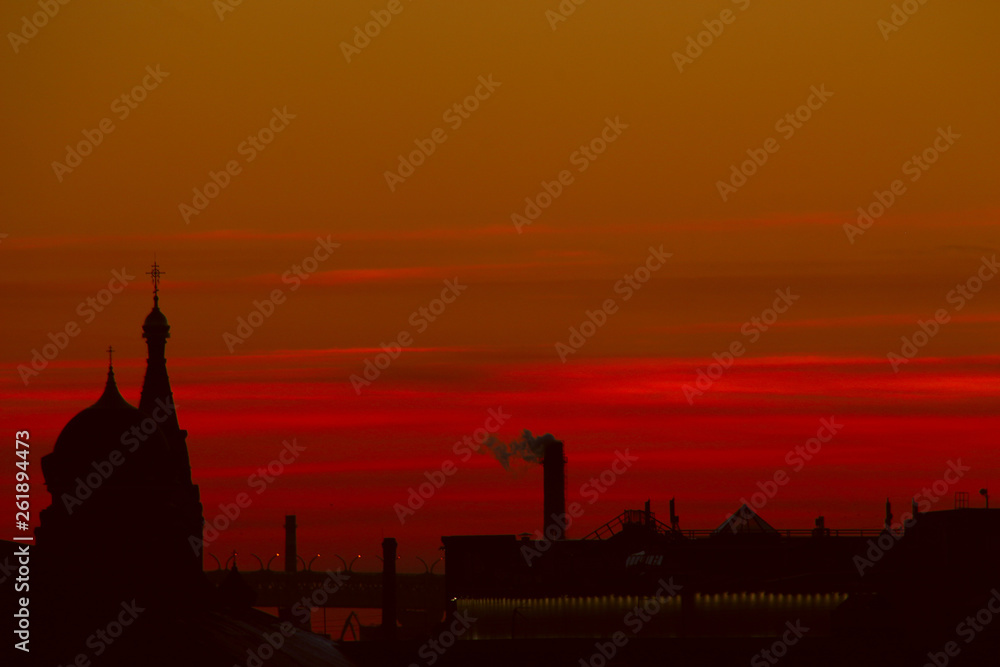 Cityscape: silhouettes of churches, industrial pipes and city roofs at sunset