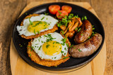 Traditional potato pancakes with fried eggs, mushrooms, sausages and tomatoes served on a hot frying pan.