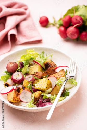 Salad with roasted potatoes, green salad leaf and radishes on a plate, pink background. Healthy low calorie summer salad