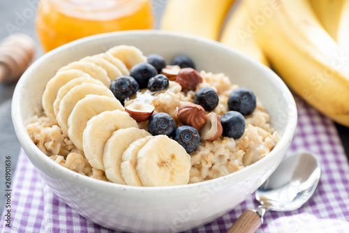 Tasty Oatmeal Porridge Bowl With Banana, Blueberry, Hazelnuts And Honey. Vegan Breakfast Food For Healthy Diet