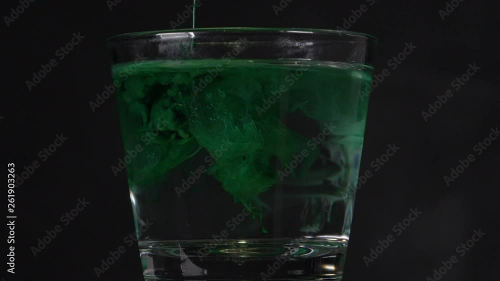 Green liquid is poured into water. Green color ink is being dissolved in a glass of water and creating abstract background. Colored acrylic cloud abstract. Ink swirling underwater. Close up view Green liquid is poured into water. Green color ink is being dissolved in a glass of water and creating abstract background. Colored acrylic cloud abstract. Ink swirling underwater. Close up view
