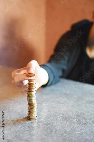 Young man hand puts coin on money stack on grey table. Personal finance, finance accounting and management, money savings or thrifty concept.