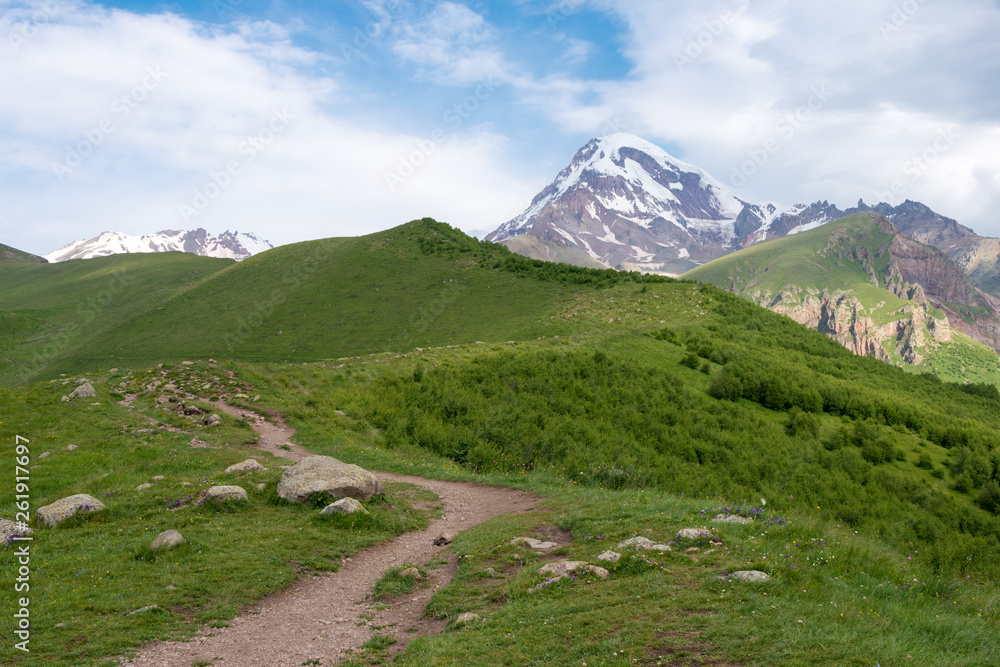 Fototapeta premium Kazbegi, Georgia - Jun 29 2018: Mountain range on a hiking trail from Gergeti Trinity Church to Gergeti Glacier. a famous landscape in Kazbegi, Mtskheta-Mtianeti, Georgia.