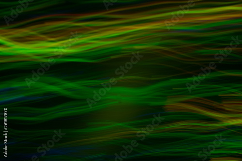 Blurry horizontal wavy lines. Green lights in motion on dark background. Bokeh lens flare glow.