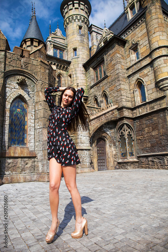 Full-length portrait young beautiful girl in summer dress posing against the backdrop of an old castle in the Gothic style
