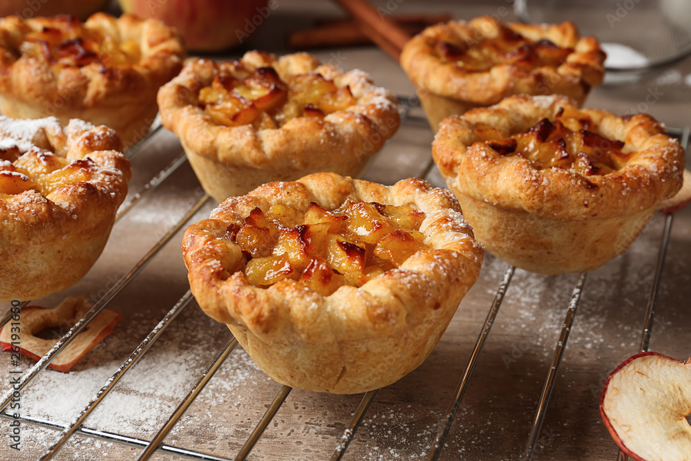 Cooling rack with tasty apple pies on table