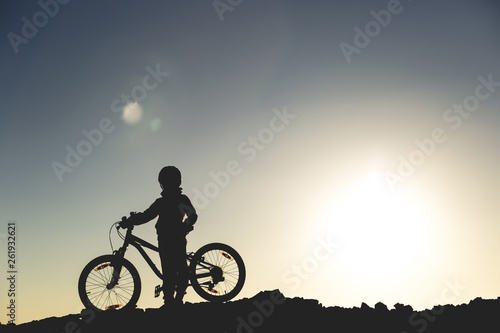 Silhouette of a little girl with a bicycle at sunset
