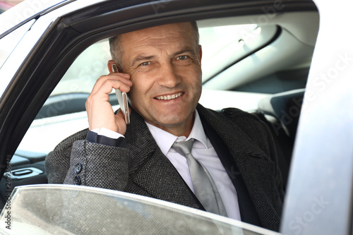 Handsome mature businessman talking by phone in car