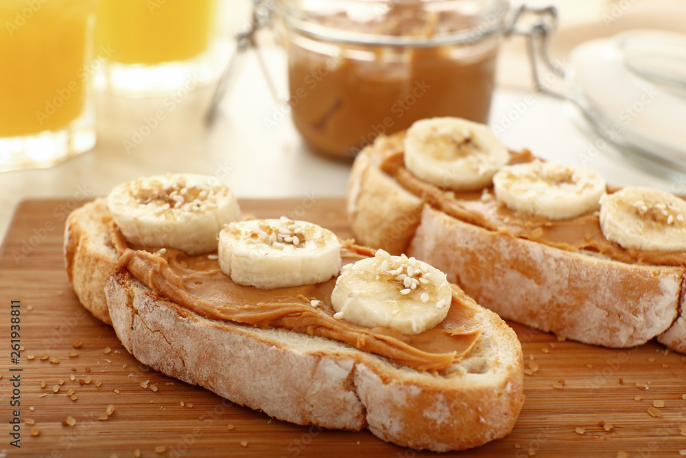 Bread with tasty peanut butter and banana on wooden board, closeup