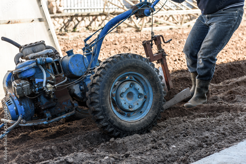 Obraz premium A man working in the field. A man plows the land with motor cultivator