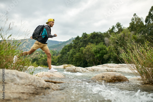 Traveler running through shallow rocky river on nature background