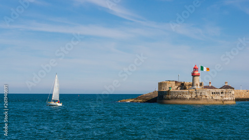 Sail boat leaving the harbor. The lighthouse of Dun Laoghaire East Pier on a sunny summer day. Seascape in Dublin, Ireland. © Gabriel