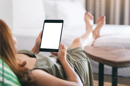 Mockup image of a woman holding and using tablet pc with blank screen while relaxing and lying on the bed