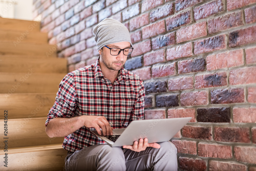 Portrait of modern hipster sitting on stairs and working on his laptop. Portrait of modern hipster sitting on stairs and working on his laptop.