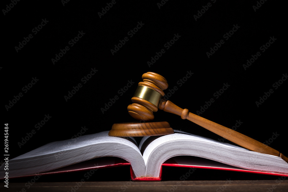 Legal law and justice concept. Judges gavel with soundboard on big opened law book against black background. Legal law and justice concept. Judges gavel with soundboard on big opened law book against black background.