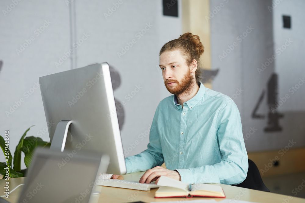 Portrait of bearded IT specialist using computer sitting at desk in office, copy space Portrait of bearded IT specialist using computer sitting at desk in office, copy space