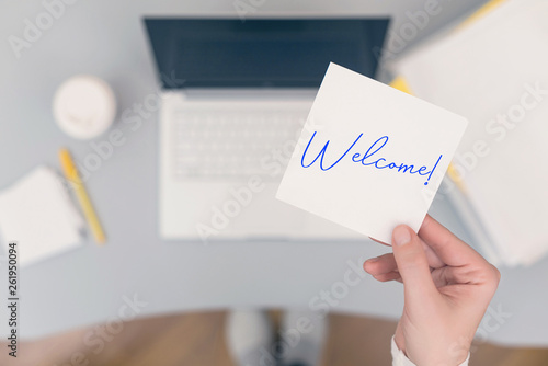 Woman clerk sitting holding note paper sticker with Welcome word. Business concept. Concept. photo