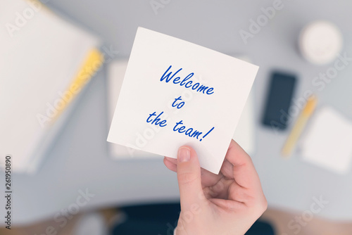 Woman clerk sitting holding note paper sticker with welcome to the team phrase. Business concept. Concept. photo