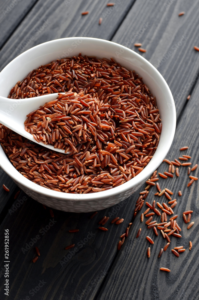 red rice in a ceramic bowl with spoon against dark wooden background red rice in a ceramic bowl with spoon against dark wooden background
