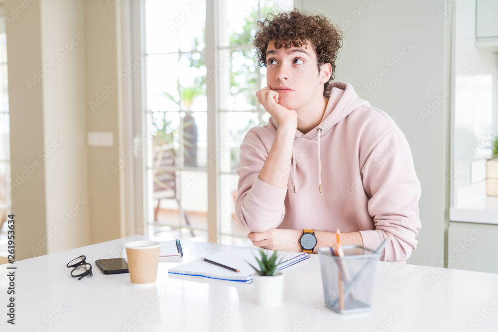 Young student man writing on notebook and studying with hand on chin thinking about question, pensive expression. Smiling with thoughtful face. Doubt concept. Young student man writing on notebook and studying with hand on chin thinking about question, pensive expression. Smiling with thoughtful face. Doubt concept.