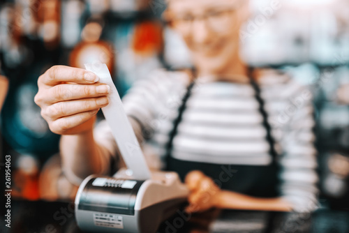 Close up of smiling Caucasian female worker with short blonde hair and eyeglasses using cash register while standing in bicycle store.