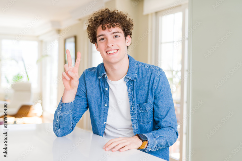 Young handsome man wearing casual denim jacket at home smiling with happy face winking at the camera doing victory sign. Number two. Young handsome man wearing casual denim jacket at home smiling with happy face winking at the camera doing victory sign. Number two.