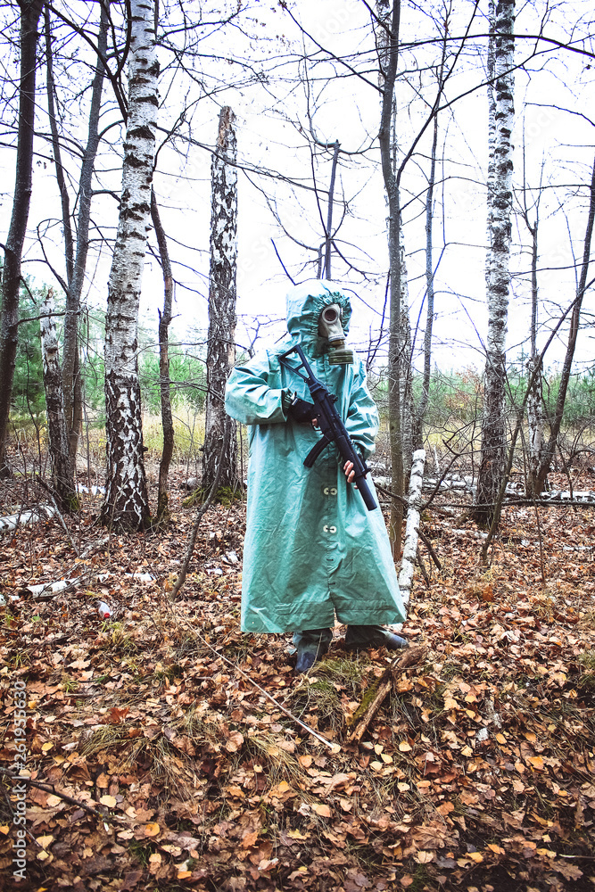 Stalker, a man in a gas mask and special chemical protection, green cloak. With a gun in his hand, walking in the forest Stalker, a man in a gas mask and special chemical protection, green cloak. With a gun in his hand, walking in the forest