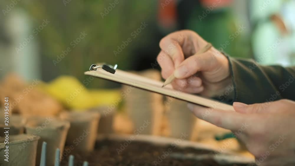 Gardener writing notes on clipboard note paper, preparation for seed planting