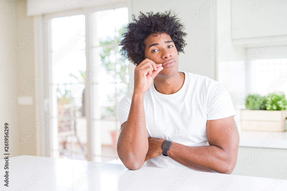 Young african american man wearing casual white t-shirt sitting at home mouth and lips shut as zip with fingers. Secret and silent, taboo talking Young african american man wearing casual white t-shirt sitting at home mouth and lips shut as zip with fingers. Secret and silent, taboo talking