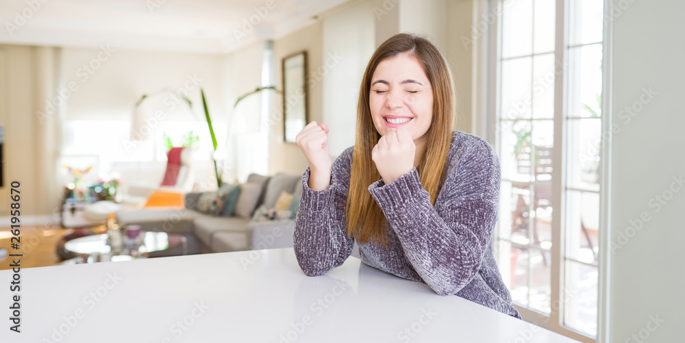 Beautiful young woman at home very happy and excited doing winner gesture with arms raised, smiling and screaming for success. Celebration concept.