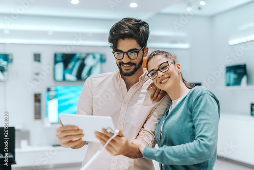 Young attractive multicultural couple with eyeglasses trying out tablet in tech store.