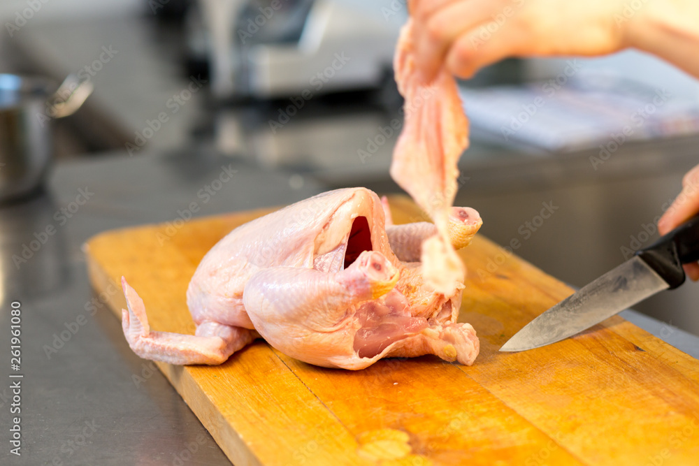 A woman chef  caucasian cuts raw chicken. Master class. Cook's hand with a knife close-up on the background of the kitchen. The background is blurred