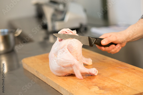 A person chef  caucasian cuts raw chicken. Master class. Cook's hand with a knife close-up on the background of the kitchen.